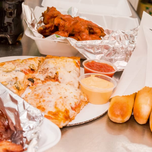Bob's Tu Your Door Pizza slices, buffalo wings, breadsticks, and dipping sauces on a metal counter.