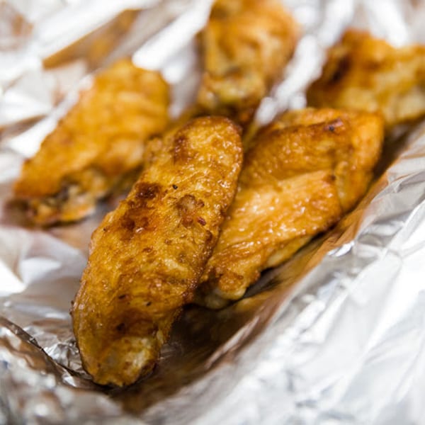 Golden brown chicken wings from Bob's Tu Your Door Pizza, nestled in crinkled aluminum foil.